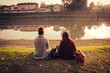 © ylenia cancelli - two young female friends sitting on the bank of a river while using their smartphones
