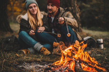 Traveler couple camping and roasting marshmallows over the fire in the forest after a hard day. Concept of trekking, adventure and seasonal vacation.