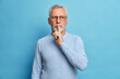 © wayhome.studio  - Photo of mysterious bearded man makes silence gesture has thoughtful expression asks to be quiet tells secret wears casual jumper and optical glasses isolated over blue background. Shh dont speak