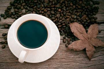 black coffee in white mug with maple leaf on wooden table in vintage style