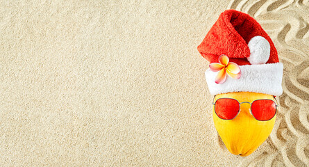 Wall Mural - Fresh yellow coconut in a red Santa Christmas hat with red sunglasses on sand, top view