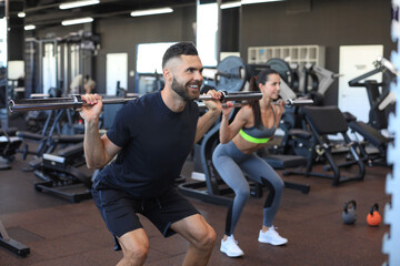 Man and woman with barbell flexing muscles in gym.