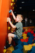 Determined boy going up a climbing wall on a side of soft cube pool