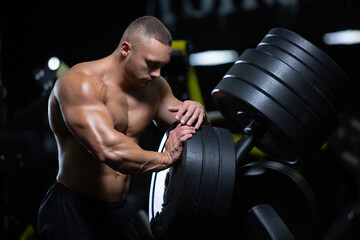 Wall Mural - Young muscular athlete man of model appearance is having rest after working out training muscles in the gym standing next to the discs