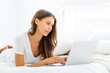 © Nata Bene - Young woman working at home laying on bed in pajamas, shopping online. Female in bedroom typing on laptop, distance learning for students, surfing Internet in morning after waking up