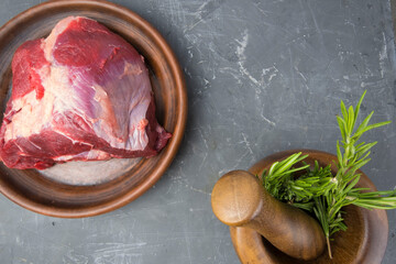 fresh and raw piece of beef meat prepared for grilling or barbecue and fresh organic rosemary in a mortar. delicious whole piece of red meat on a clay plate.