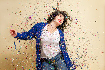 Laughing young brunette girl sprinkled with confetti. Festive mood. New Year's and Christmas. Yellow background.