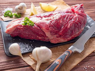 Wall Mural - A piece of fresh raw beef lies on parchment surrounded by spices, herbs and vegetables. The knife is lying nearby. Side view. Food composition