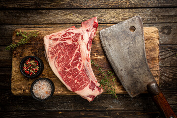 raw fresh meat t-bone beef steak and butcher knife on wooden background, top view