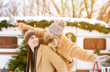 Cheerful millennial couple having fun outside at winter camping, woman piggybacking boyfriend