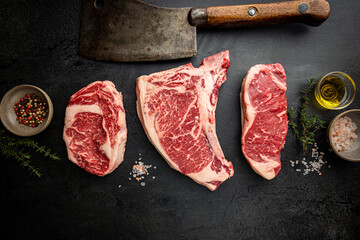 Wall Mural - Variety of Fresh Raw Black Angus Prime Meat Steaks T-bone, New York, Ribeye and seasoning on black background, top view