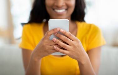 Wall Mural - Cropped view of positive black lady holding modern smartphone indoors, chatting with friends or sending email