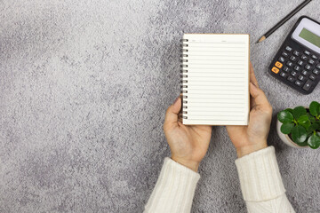 Wall Mural - A woman's hand holding a notebook with pencil and calculator on the desk.- Business concept.