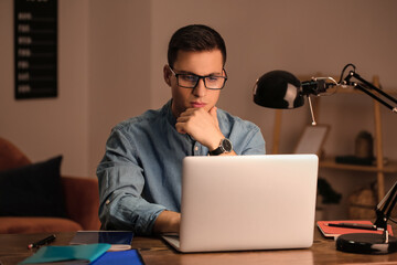 Young man working on laptop in office late in evening