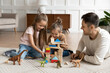 © fizkes - Little daughters play with dad, family sit on carpet on warm floor in living room, daddy enjoy playtime with kids build tower castle use wooden colorful blocks, free time at home with children concept