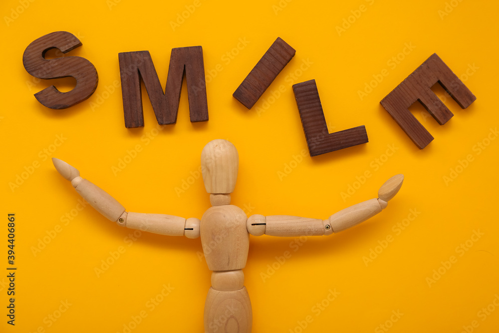 Wooden mannequin with word SMILE on color background