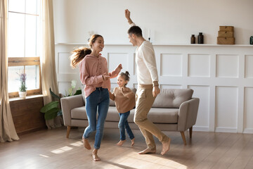 cheery couple dancing with little daughter barefoot on wooden laminate floor with underfloor heating