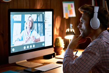 Serious male student wearing headphones taking online course training, watching webinar, remote university class, virtual learning with social distance web teacher, tutor or coach using computer.