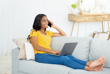 Wall Mural - Joyful African American woman communicating with someone on cellphone and laptop from home