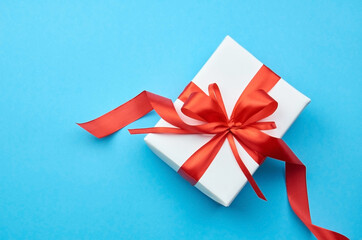 White gift box with red ribbon bow on blue background