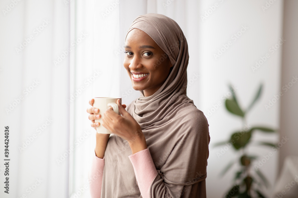 Black Muslim woman in traditional hijab drinking hot aromatic coffee ...