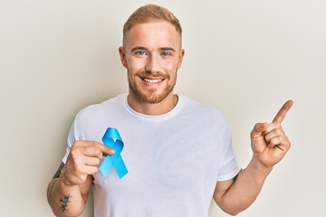 Wall Mural - Young caucasian man holding blue ribbon smiling happy pointing with hand and finger to the side