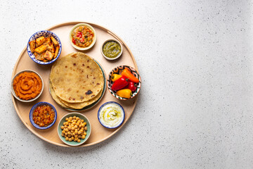 Wall Mural - Indian Thali - selection of various dishes served on round wooden platter, white table. Assorted Indian vegetarian meze with chapati bread, paneer, dal, chutney in bowls. Top view, space for text