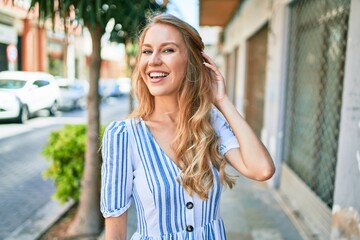 Young beautiful caucasian woman with blond hair smiling happy and cheerful walking on sunny day