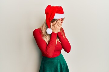 Poster - Beautiful caucasian woman wearing christmas costume and hat with sad expression covering face with hands while crying. depression concept.