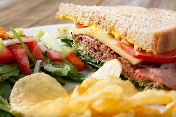 A closeup view of a roast beef  sandwich and salad entree, with a side of potato chips.