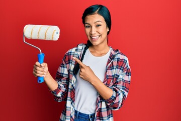 Wall Mural - Beautiful hispanic woman holding roller painter smiling happy pointing with hand and finger