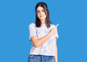 Young beautiful girl wearing casual t shirt pointing with hand finger to the side showing advertisement, serious and calm face