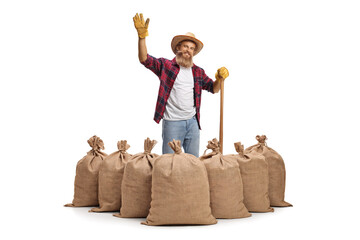 Poster - Young bearded farmer with a shovel standing behind burlap sacks and waving at camera