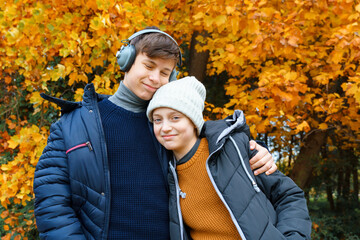 Wall Mural - portrait of a teenager boy and girl listening to music by headphones, relaxing in autumn city park, bright yellow maple leaves as background