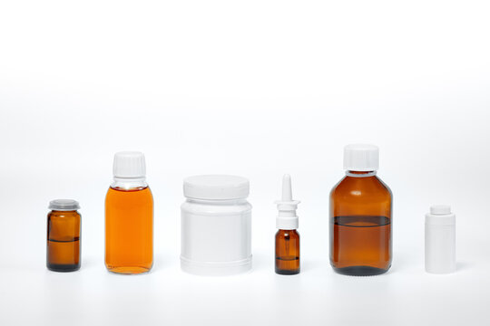 Wall Mural - glass jars and white plastic medical containers on a white background, medicines in syrup, tinctures, drops and sprays, different forms of medicinal products
