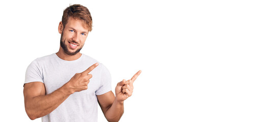 Young caucasian man wearing casual white tshirt smiling and looking at the camera pointing with two hands and fingers to the side.