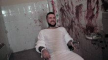 Crazy Man In Straitjacket Tied To A Chair, Killer Psychopath In A Room Smiles With Bloodied Walls Overdose