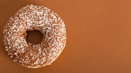 Fresh appetizing donut in chocolate glaze with coconut chips on a brown background. Close-up. copy space. Free space for text. top view