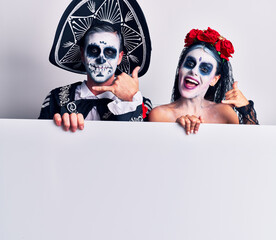 Sticker - Young couple wearing mexican day of the dead costume holding blank empty banner smiling doing phone gesture with hand and fingers like talking on the telephone. communicating concepts.