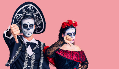 Canvas Print - Young couple wearing mexican day of the dead costume over background looking unhappy and angry showing rejection and negative with thumbs down gesture. bad expression.