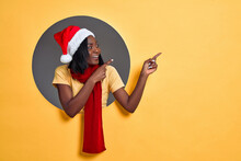 Young Woman Wearing Christmas Hat And Scarf Pointing To Side. Christmas Sale Concept. Copy Space.