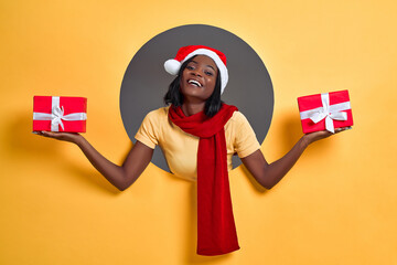 Christmas afro woman holding two gift boxes in hand, isolated circle in a yellow background. Christmas gift concept.