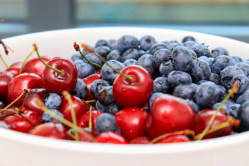 Raw juicy berries of sweet cherry and blueberry in a white ceramic dish, close up