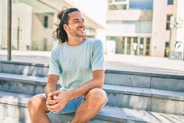 Sticker - Young hispanic man smiling happy looking to the side and sitting on the stairs.