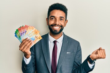 Poster - Handsome young hispanic business man holding swiss franc banknotes celebrating achievement with happy smile and winner expression with raised hand