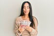 © Krakenimages.com - Young beautiful hispanic girl holding 10 colombian pesos banknotes making fish face with mouth and squinting eyes, crazy and comical.