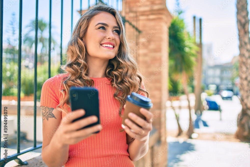 Young blonde girl smiling happy using smartphone and drinking take away coffee at the city.