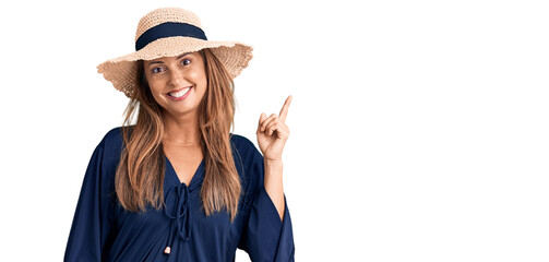 Poster - Middle age hispanic woman wearing summer hat with a big smile on face, pointing with hand and finger to the side looking at the camera.