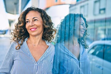 Wall Mural - Middle age hispanic woman smiling happy leaning on the wall at the city.