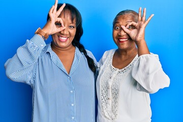 Hispanic family of mother and daughter hugging together with love smiling happy doing ok sign with hand on eye looking through fingers